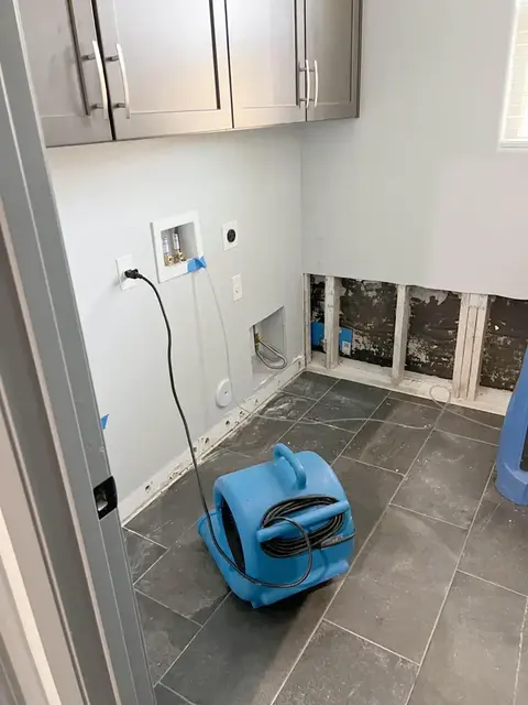Air mover drying a laundry room after the wet drywall was cut out